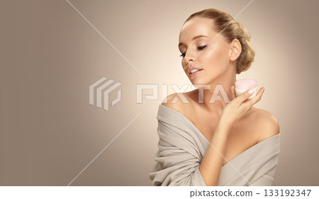 Beautiful caucasian blonde woman shows face cream on palm of hand over beige isolated with free copy space. Beautiful caucasian blonde woman shows face cream on palm of hand over beige isolated with free copy space. 133192347