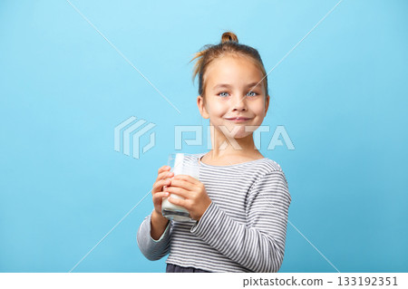 Beautiful little girl with glass of milk, stands on blue isolated. 133192351