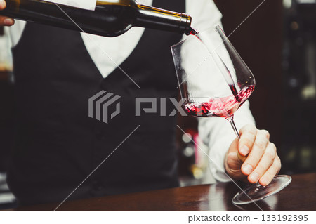 Close-up photo, sommelier pours red wine to glass on bar counter background. Close-up photo, sommelier pours red wine to glass on bar counter background. 133192395