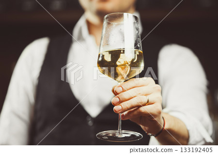 Bartender at the bar hands the camera a glass of white wine, close-up. Bartender at the bar hands the camera a glass of white wine, close-up. 133192405