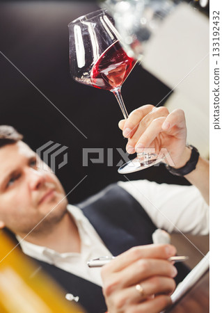 Skilled male sommelier looks carefully at drink in stem glass. Skilled male sommelier looks carefully at drink in stem glass. 133192432