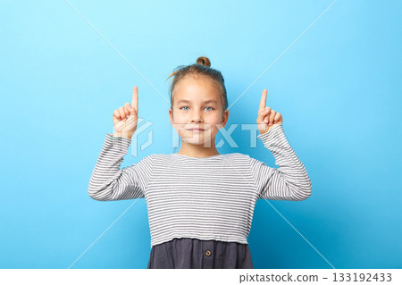 Portrait of a beautiful child girl pointing fingers up at copyspace isolated over blue. Portrait of a beautiful child girl pointing fingers up at copyspace isolated over blue. 133192433