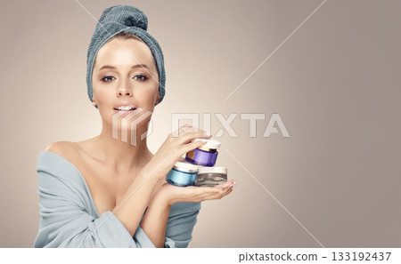 Pretty woman with clean fresh skin hold a different of face care creams, wearing in bathrobe and towel on head. Cosmetology, beauty and spa. Concept of skin rejuvenation without surgery. Pretty woman with clean fresh skin hold a different of face care creams, wearing in bathrobe and towel on head. Cosmetology, beauty and spa. Concept of skin rejuvenation without surgery. 133192437