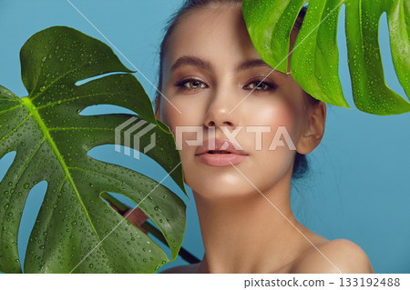 Seductive model holds palm leaves with water drops on blue Seductive model holds palm leaves with water drops on blue 133192488