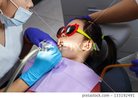 Child Girl Wearing Heart-Shaped Glasses During Dental Treatment at Pediatric Clinic Child Girl Wearing Heart-Shaped Glasses During Dental Treatment at Pediatric Clinic 133192491