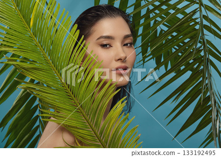 Well groomed woman peeks out from behind palm leaves. Well groomed woman peeks out from behind palm leaves. 133192495
