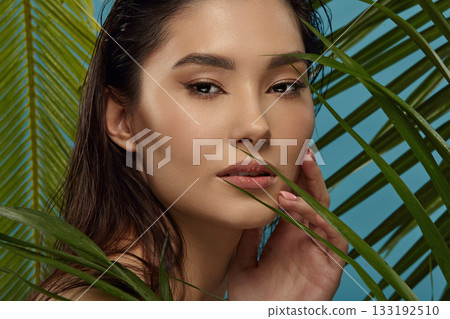 Beautiful girl with cat eyes stands between exotic plants leaves. 133192510