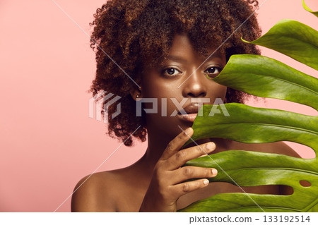 Curious black girl peeks out from behind monstera leaf. Curious black girl peeks out from behind monstera leaf. 133192514