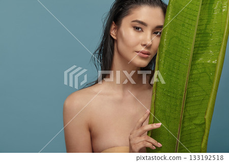 Tropical woman peeking out from behind exotic plant big leaf. 133192518