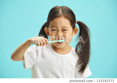 Happy asian ethnicity cute child girl use hand holds toothbrush, brushing teeth myself at morning every day standing over blue isolated background with copy space, health medical care Happy asian ethnicity cute child girl use hand holds toothbrush, brushing teeth myself at morning every day standing over blue isolated background with copy space, health medical care 133192571