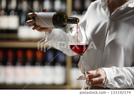 Female bartender pouring red wine to glass for tasting, close up. Female bartender pouring red wine to glass for tasting, close up. 133192574