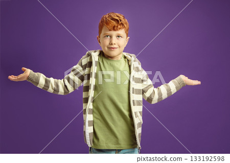 Puzzled and ignorant little red-haired boy shrugs his shoulders, symbolizing lack of knowledge, showing illiteracy wearing in casual clothes standing against violet isolated background Puzzled and ignorant little red-haired boy shrugs his shoulders, symbolizing lack of knowledge, showing illiteracy wearing in casual clothes standing against violet isolated background 133192598