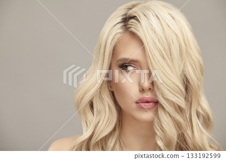 Blonde woman with long wavy hair looks aside on beige isolated background with free copy space. Blonde woman with long wavy hair looks aside on beige isolated background with free copy space. 133192599