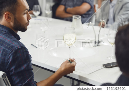 Professional looking sommelier tasting white wine from glass, analysing its taste, color, smell and acidity level. Wine expert studies wine geographic and area on winemaking lecture.  133192601