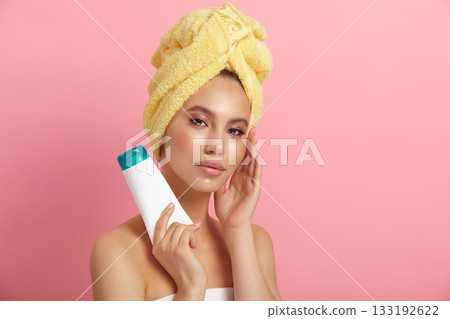 Pretty lady with towel on head holding blank tube on pink Pretty lady with towel on head holding blank tube on pink 133192622