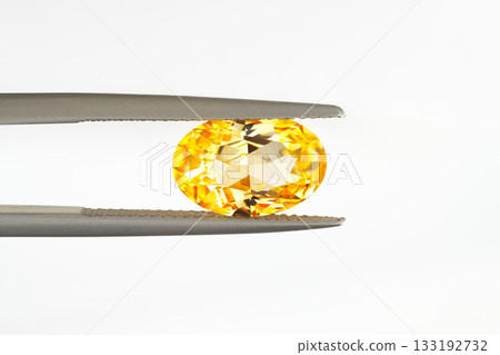 A yellow gemstone is being held up by a metal clamp 133192732
