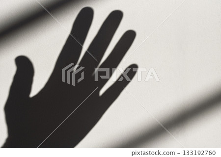 A hand casts a shadow on a wall 133192760