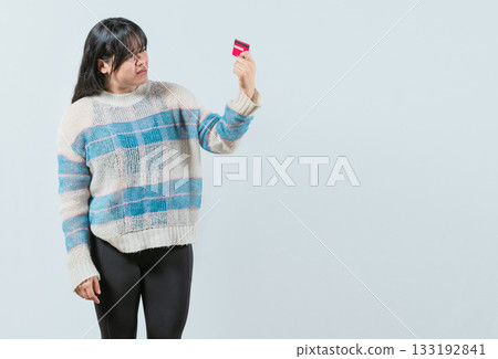 Unsure and confused young woman holding and looking at a credit card isolated. Confused asian girl holding a debit card 133192841