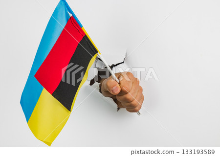 Hand holding flag of Ukraine breaking through a wall Hand holding flag of Ukraine breaking through a wall 133193589