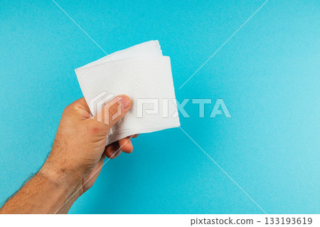 Hand holding a stack of white napkins against a blue background Hand holding a stack of white napkins against a blue background 133193619