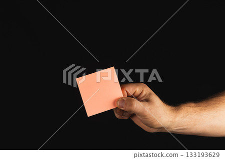 Hand holding a pink note against a dark background 133193629