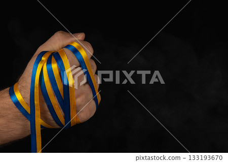 Strong hand holding blue and yellow ribbons in solidarity and support Strong hand holding blue and yellow ribbons in solidarity and support 133193670