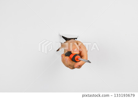 Hand holds screwdriver through a torn wall, showing home repair activity 133193679