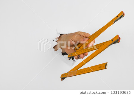 Hand holding measuring tools through hole in a wall Hand holding measuring tools through hole in a wall 133193685