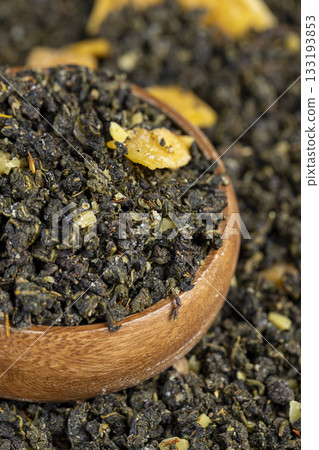 green large-leaf aromatic tea with the addition of dried ripe peach fruits in a wooden bowl , dried high-quality leaf tea poured into a bowl 133193853