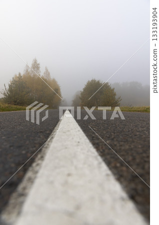 a narrow country road with yellowing trees on the edge of the road in the autumn season, cloudy weather with a gray sky, thick fog in the morning due to climate change a narrow country road with yellowing trees on the edge of the road in the autumn season, cloudy weather with a gray sky, thick fog in the morning due to climate change 133193904