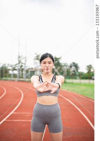 Young Asian woman stretching on athletic track, preparing for workout, wearing sportswear, focusing on fitness and athletic training outdoors 133193967