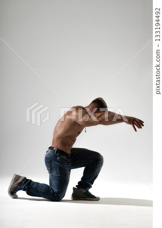 An athletic man showcases his strength in a studio kneeling with arms extended forward. His focused expression highlights determination while highlighting a fit physique. An athletic man showcases his strength in a studio kneeling with arms extended forward. His focused expression highlights determination while highlighting a fit physique. 133194492