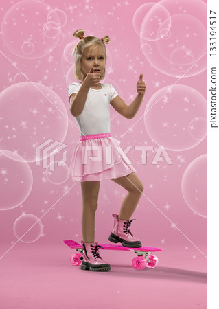 small blonde girl stands confidently on a pink skateboard in a studio setting. She is wearing a white shirt pink skirt and boots. Bubbles surround her in the playful scene. small blonde girl stands confidently on a pink skateboard in a studio setting. She is wearing a white shirt pink skirt and boots. Bubbles surround her in the playful scene. 133194517