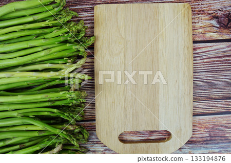 Bunch of fresh green asparagus stems with cutting wooden board on wooden background 133194876