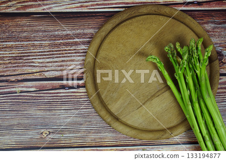 Bunch of fresh green asparagus stems with cutting wooden board on wooden background 133194877