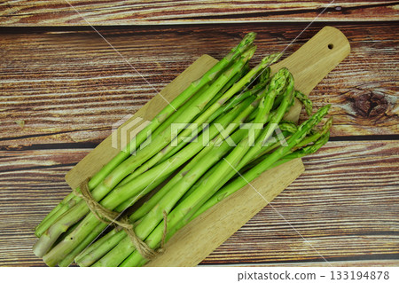 Bunch of fresh green asparagus stems with cutting wooden board on wooden background 133194878