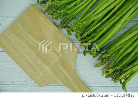 Bunch of fresh green asparagus stems with cutting wooden board on wooden background Bunch of fresh green asparagus stems with cutting wooden board on wooden background 133194882