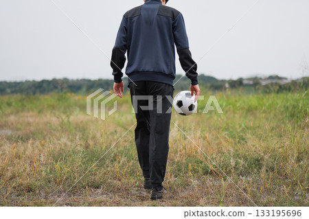 Rear view of a man kicking a soccer ball 133195696