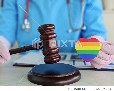 Health care professional holds rainbow heart and gavel representing LGBTQ rights and justice in medical settings Health care professional holds rainbow heart and gavel representing LGBTQ rights and justice in medical settings 133195725