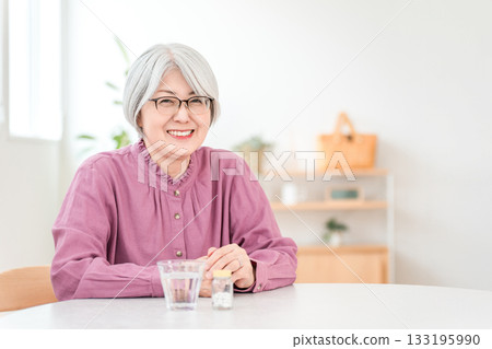 Gray-haired senior woman holding medicine, supplements, and oral medication 133195990