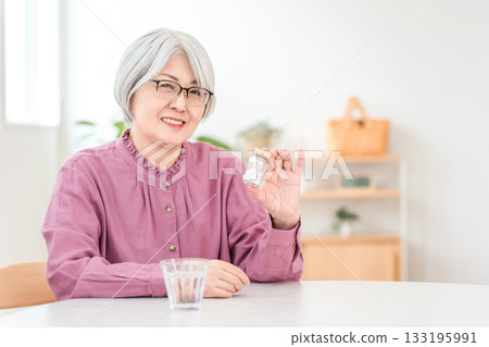 一位頭髮花白的老婦人手裡拿著藥品、保健品和口服藥。 一位頭髮花白的老婦人手裡拿著藥品、保健品和口服藥。 133195991