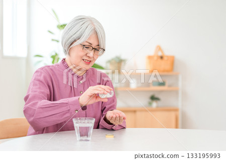 Gray-haired senior woman holding medicine, supplements, and oral medication 133195993