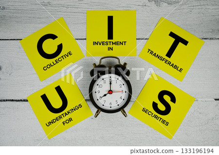 UCITS Undertakings for Collective Investment in Transferable Securities with alarm clock on wooden background 133196194