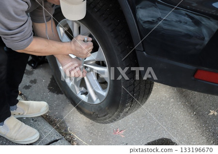 Changing tires by yourself: A man tightening the wheel nuts on studless tires 133196670