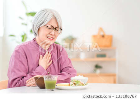 A gray-haired senior woman choking while eating (aspiration pneumonia, swallowing disorder) A gray-haired senior woman choking while eating (aspiration pneumonia, swallowing disorder) 133196767