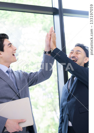 Two smiling businessmen high-fiving to celebrate success and achievements. A positive image of project success. Two smiling businessmen high-fiving to celebrate success and achievements. A positive image of project success. 133197059