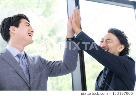 Two smiling businessmen high-fiving to celebrate success and achievements. A positive image of project success. Two smiling businessmen high-fiving to celebrate success and achievements. A positive image of project success. 133197060