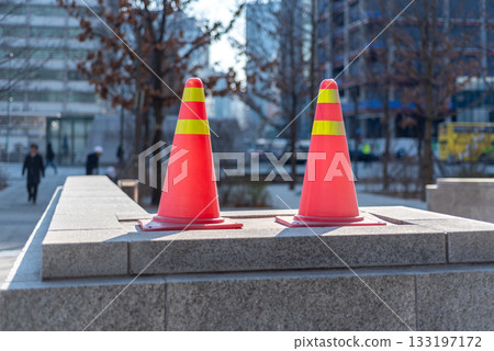 Two bright orange traffic cones with yellow stripes placed on a stone surface in an urban setting in Seoul, South Korea 133197172