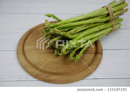 Bunch of fresh green asparagus stems with cutting wooden board on wooden background Bunch of fresh green asparagus stems with cutting wooden board on wooden background 133197295