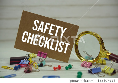 Safety Checklist text on paper card with magnifying glass and stationary on wooden background 133197551